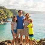 Une famille souriante profite d'une vue panoramique sur une plage tropicale au coucher du soleil.