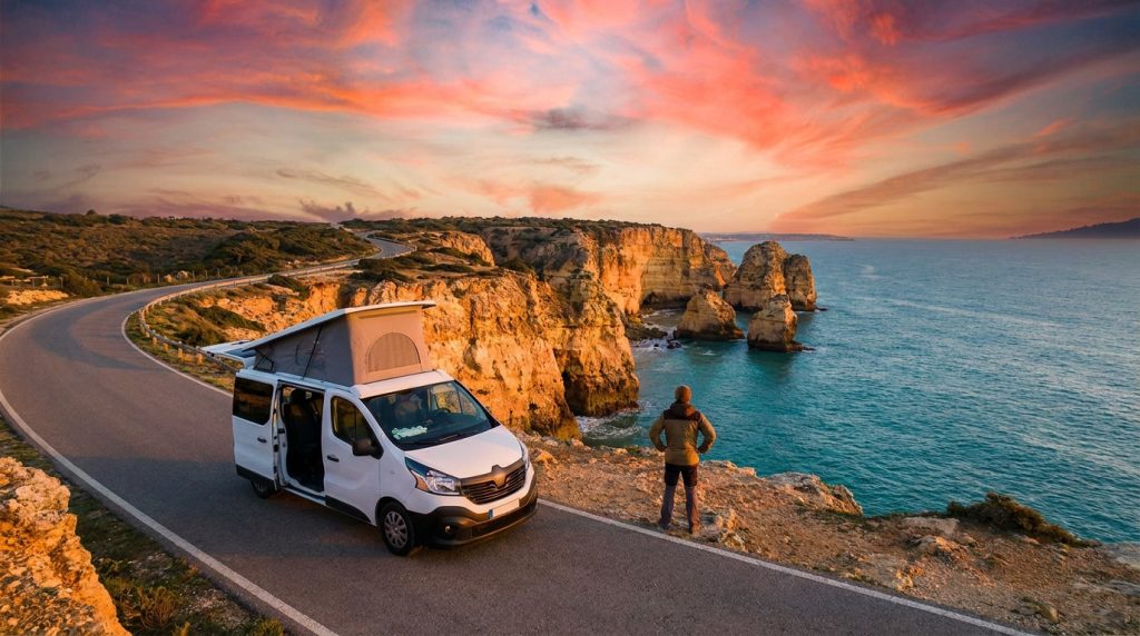 Un van aménagé garé sur une route côtière au Portugal avec un homme admirant le coucher de soleil sur les falaises.
