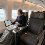 Un passager assis près du hublot dans un avion regarde le plan de cabine sur une tablette pour choisir sa place.