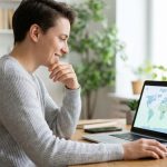 Personne souriante utilisant un ordinateur portable pour rechercher des vols sur une carte du monde.