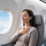 Une femme détendue dans un avion, la main sur le cœur, près du hublot avec une vue sur les nuages.