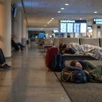 Des voyageurs dorment sur les sièges et le sol d'un hall d'aéroport la nuit avec leurs bagages autour d'eux.