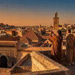 Deux personnes en djellabas admirent le coucher de soleil sur les toits d'une ville historique marocaine.