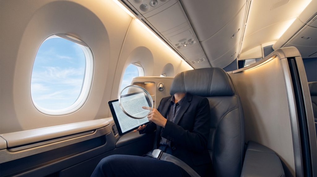 Une personne en costume examine une tablette avec une loupe dans la cabine confortable d'un avion.
