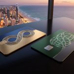 Deux cartes de crédit haut de gamme posées sur une table face à une ville côtière au coucher du soleil.