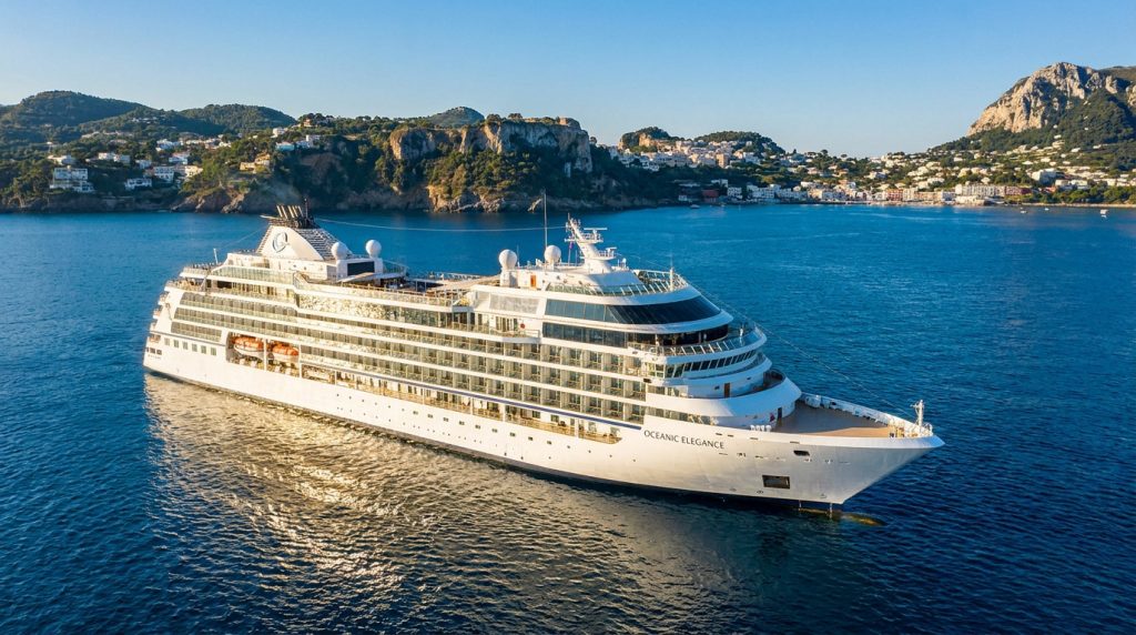 Un navire de croisière luxueux nommé Oceanic Elegance navigue sur une mer bleue près d'une côte montagneuse.