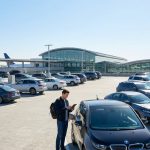 Un homme debout sur le toit d'un parking d'aéroport avec de nombreuses voitures garées et un avion en arrière-plan.