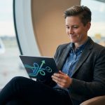 Une voyageuse souriante consulte une tablette dans un aéroport, avec un avion visible en arrière-plan.