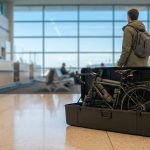 Un voyageur debout à l'aéroport avec un vélo de route protégé dans une valise rigide ouverte.
