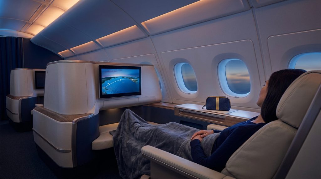 Passagère détendue dans un siège-lit privé en classe affaires Delta avec écran multimédia et vue sur le ciel.