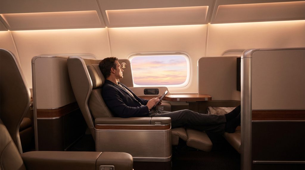 Un homme confortablement installé dans un siège de première classe d'avion, regardant le coucher de soleil par le hublot.
