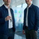 Deux hommes en veste bleue dans un aéroport, l'un tenant des clés de voiture.