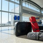 Un voyageur avec des sacs de sport volumineux dans un terminal d'aéroport avec des avions visibles en arrière-plan.
