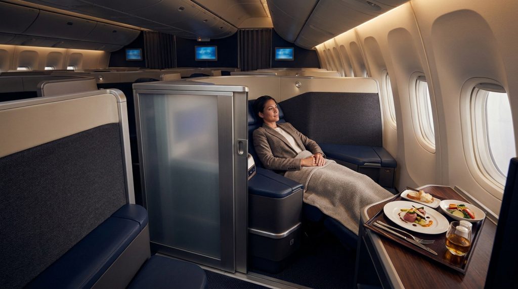 Passagère détendue dans une suite privée en classe affaires Air France, avec un repas gastronomique devant elle.