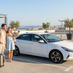 Un couple heureux récupère sa voiture de location dans un parking extérieur à Marseille avec ses bagages.