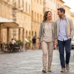 Couple souriant marchant dans une rue pavée typique d'un village italien ensoleillé.