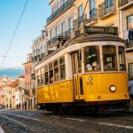 Le tramway jaune emblématique numéro 28 circulant dans une rue pavée et ensoleillée de Lisbonne avec vue sur le Tage.