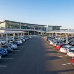 Vue aérienne d'un grand parking couvert de panneaux solaires devant un terminal d'aéroport moderne.