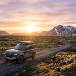 Un Land Rover Defender avec tente de toit roulant sur une piste islandaise au coucher du soleil.