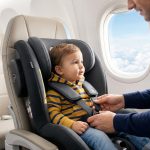 Un père ajuste le harnais du siège auto de son jeune enfant installé sur un siège d'avion près du hublot.
