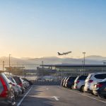 Un avion décolle au-dessus d'un parking de voitures à l'aéroport de Genève lors d'un coucher de soleil.