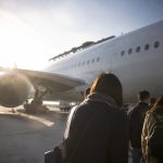 Passagers montant à bord d'un avion par une passerelle sous un ciel ensoleillé.