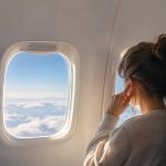 Une passagère dans un avion se touche l'oreille, gênée par la pression, en regardant par le hublot au-dessus des nuages.