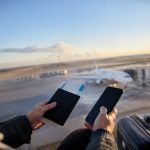Une personne tenant un passeport, un billet d'avion et un smartphone devant un avion sur le tarmac d'un aéroport.