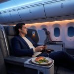 Un passager détendu en Premium Economy, dînant et utilisant une tablette devant les hublots d'un avion.