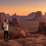 Home 43 Une randonneuse avec un sac à dos admire le coucher de soleil sur les paysages désertiques de Monument Valley.